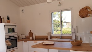 A modern kitchen with white cabinetry, a wooden countertop, and a large window.