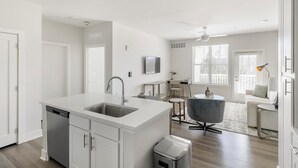 A modern kitchen with a central island, a dining area with a round table and chairs, and a living space with a sofa and a lamp.