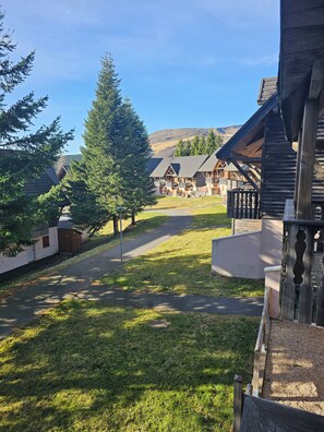 A lodge with a central walkway, surrounded by wooden cabins and a large evergreen tree.