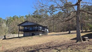 A two-story cabin with a balcony, surrounded by trees and a clear sky. - Lakefront Escape with Hot Tub (Quitman)