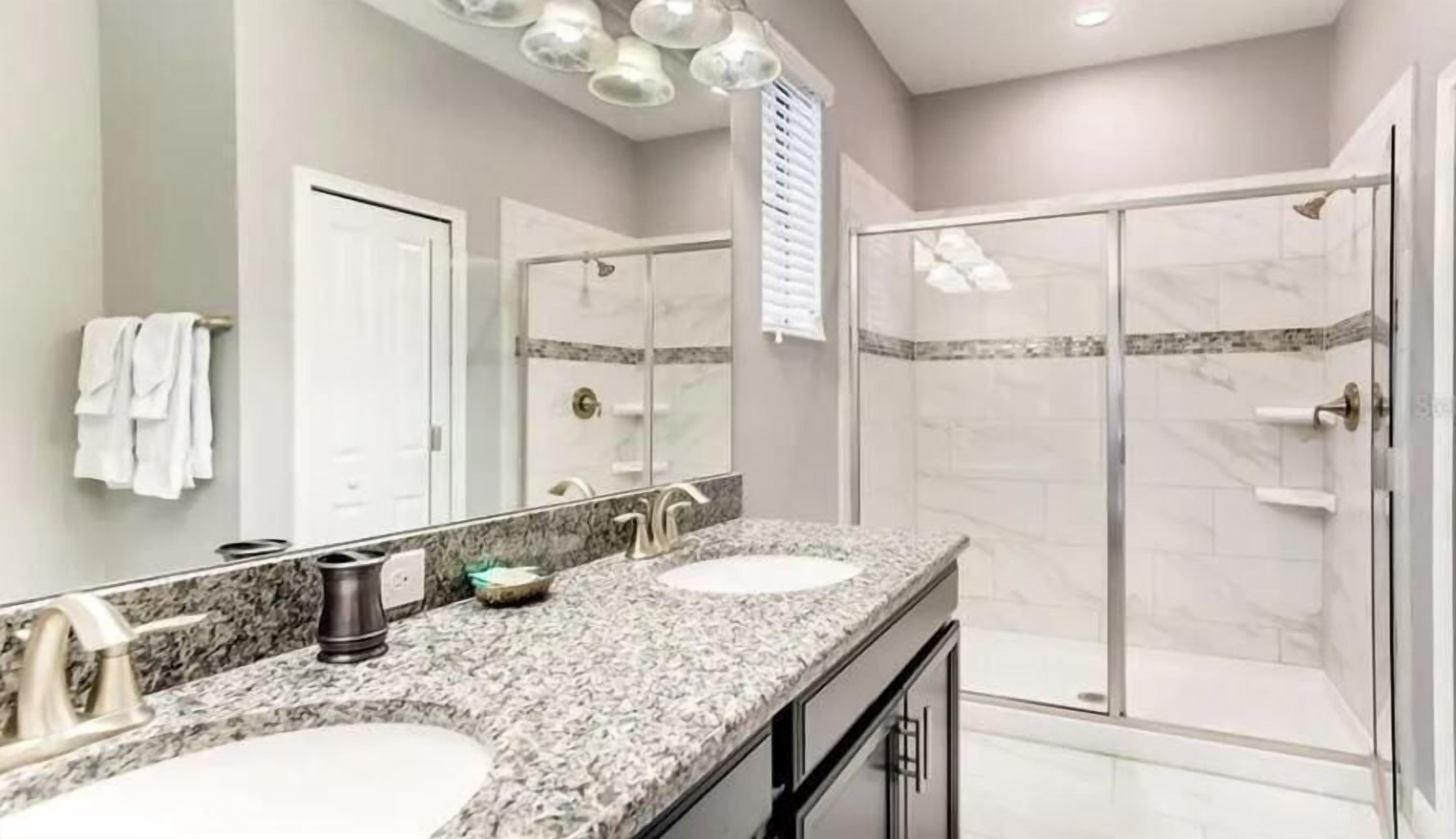 A modern bathroom with two sinks, a large mirror, and a walk-in shower.