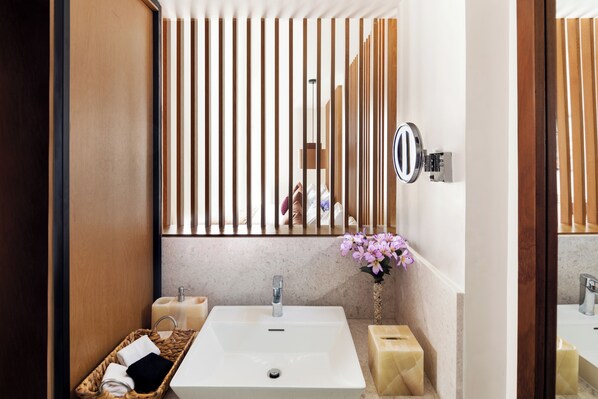 Un baño moderno con un espejo grande, dos lavamanos, un panel de pared de madera y un jarrón con flores.