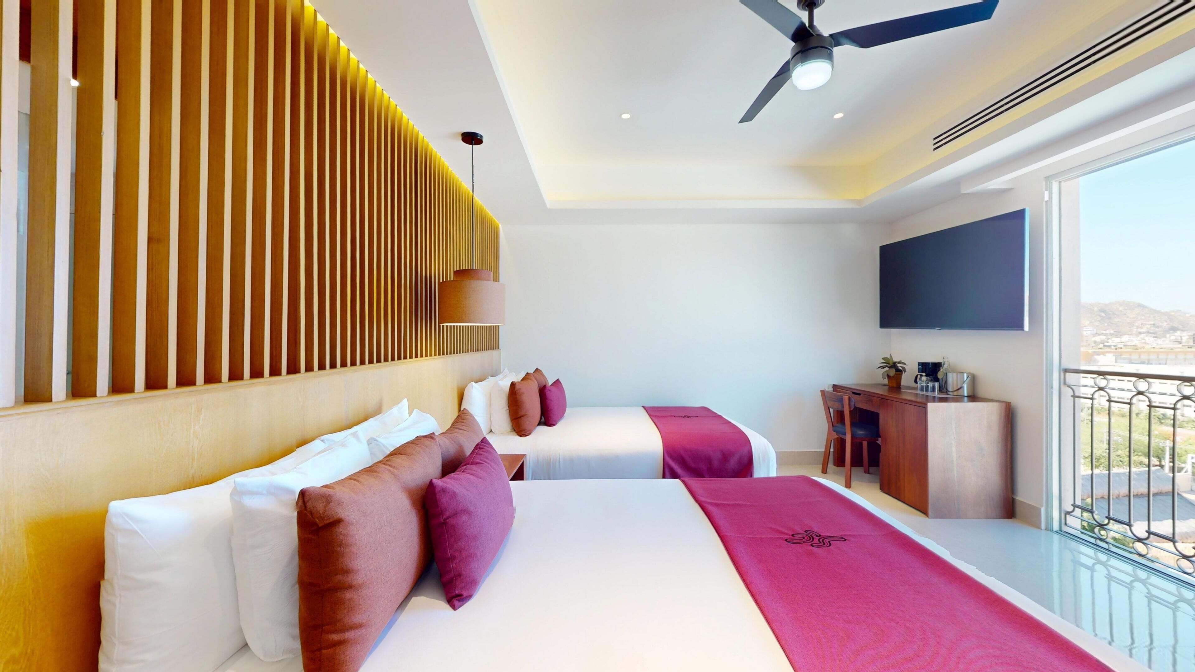 Quarto de hotel com cama, mesa de cabeceira, televisão e varanda com vista.