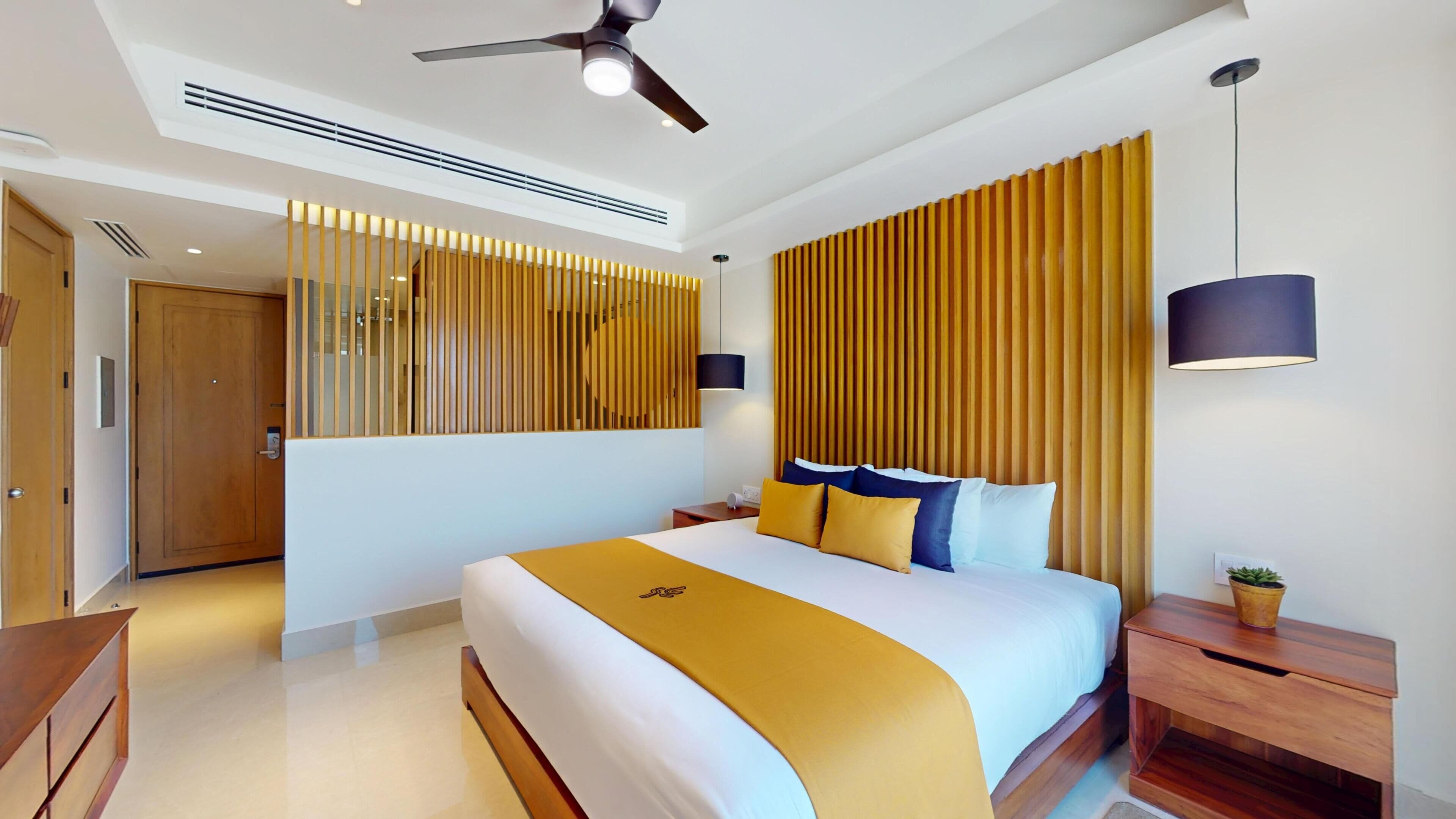 Una habitación de hotel moderna con una cama grande, un ventilador de techo, una mesita de noche y una planta en maceta.