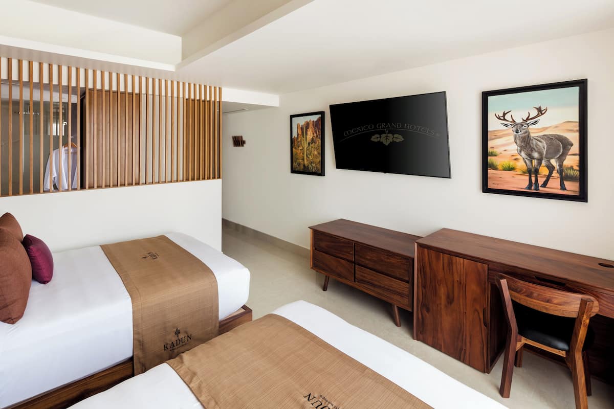 Een moderne hotelkamer met een bed, een houten bureau en een computer. Er hangen twee ingelijste foto’s aan de muur, één van een cactus en de ander van een hert.