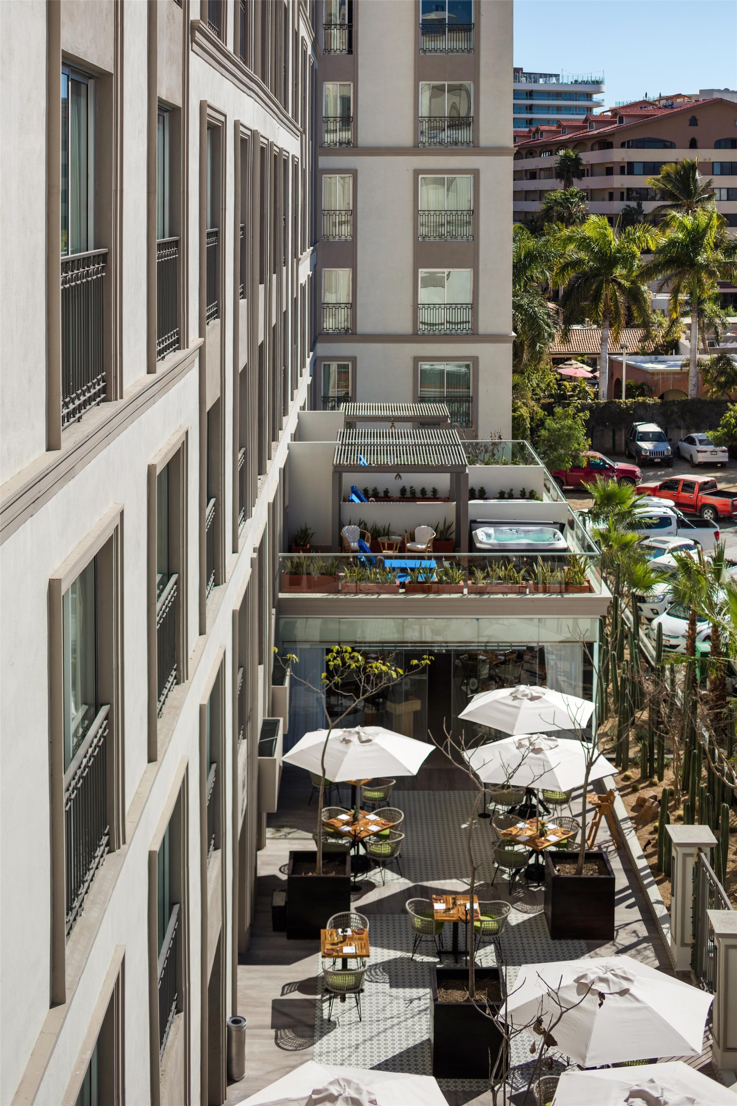 A multi-story hotel with outdoor seating, a rooftop bar, and a pool area.