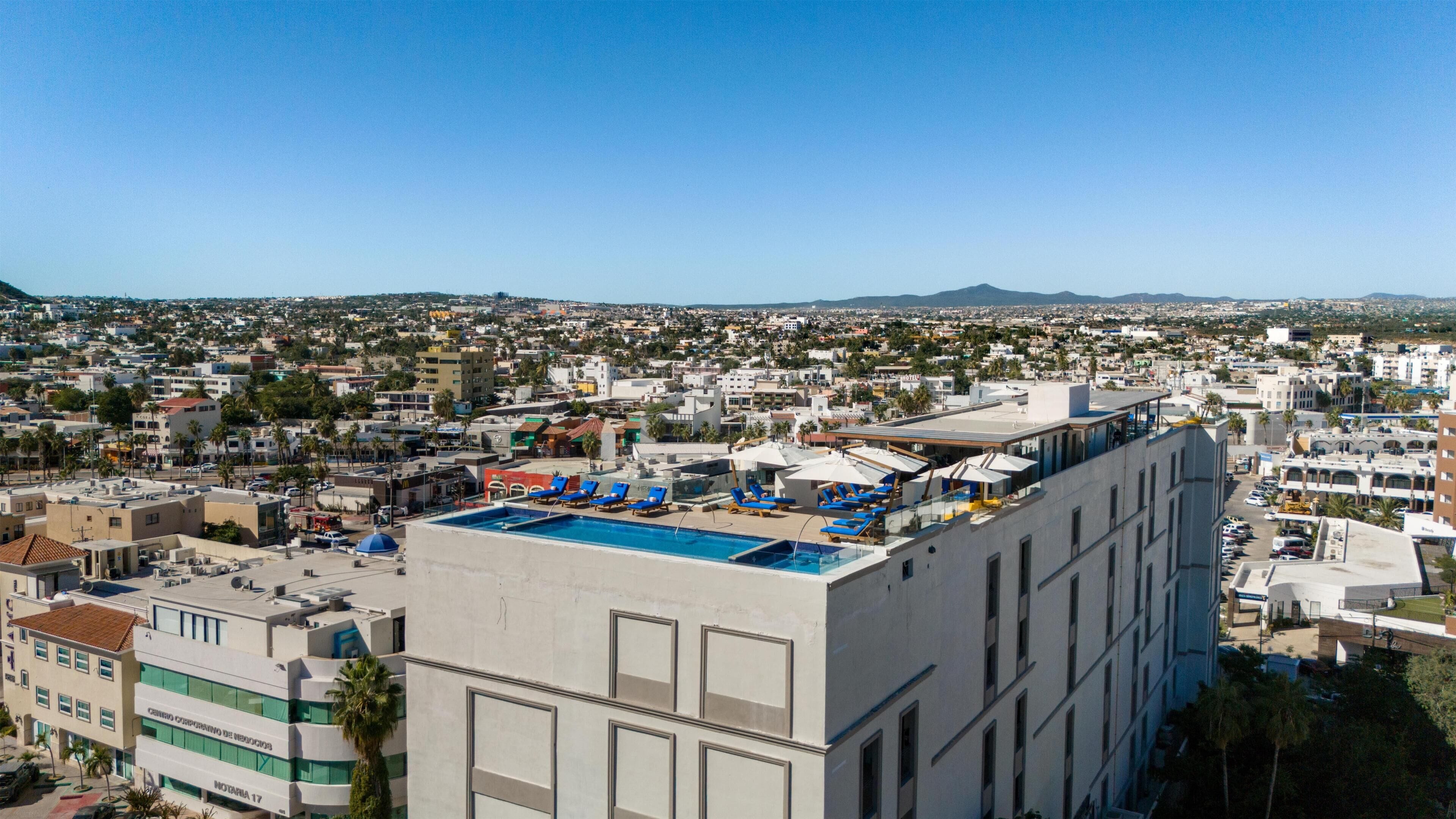 A hotel with a rooftop pool, multiple floors, and a view of a cityscape.