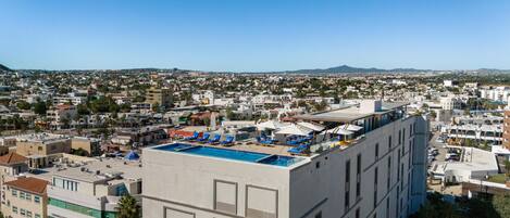 Un hotel con piscina en la azotea, varios pisos y vistas a un paisaje urbano.