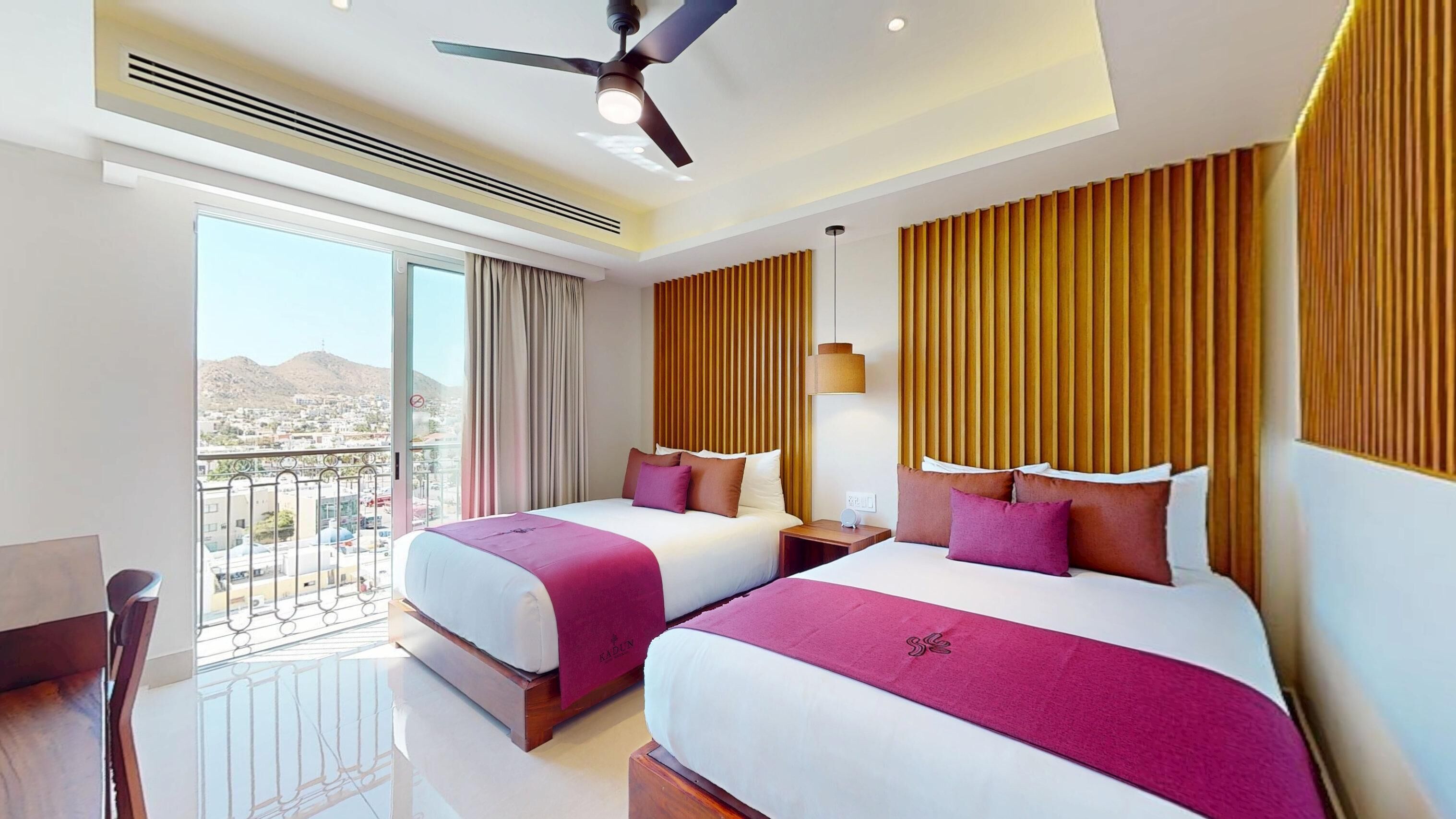 A hotel room with two beds, a balcony, a ceiling fan, and a city view.