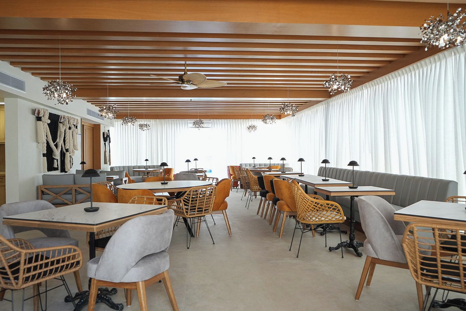 A modern dining area with multiple tables and chairs, ceiling fans, and decorative lighting fixtures.