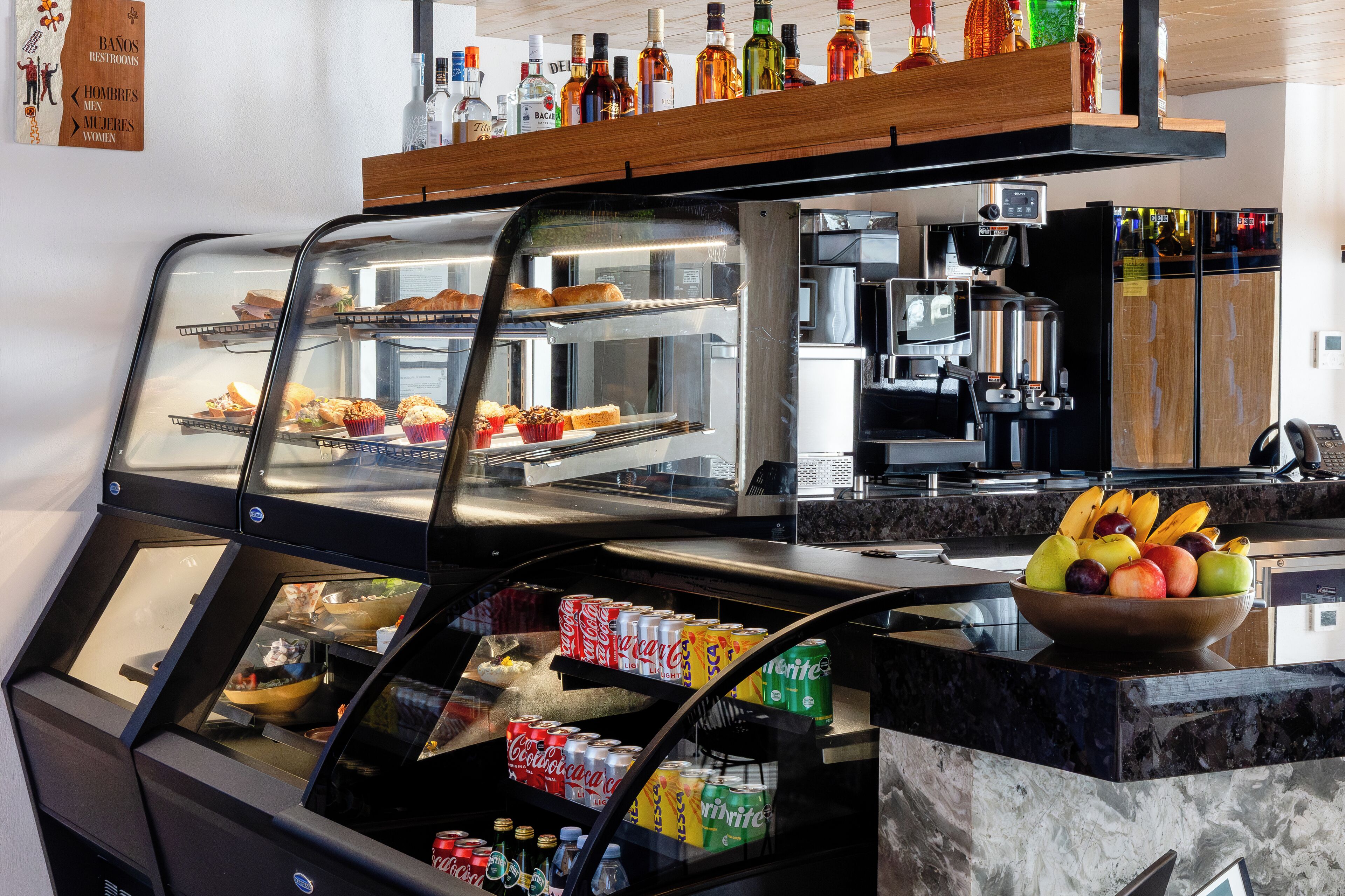 Une vitrine de boulangerie remplie de pâtisseries, un réfrigérateur contenant des boissons et un saladier de fruits sur le comptoir.