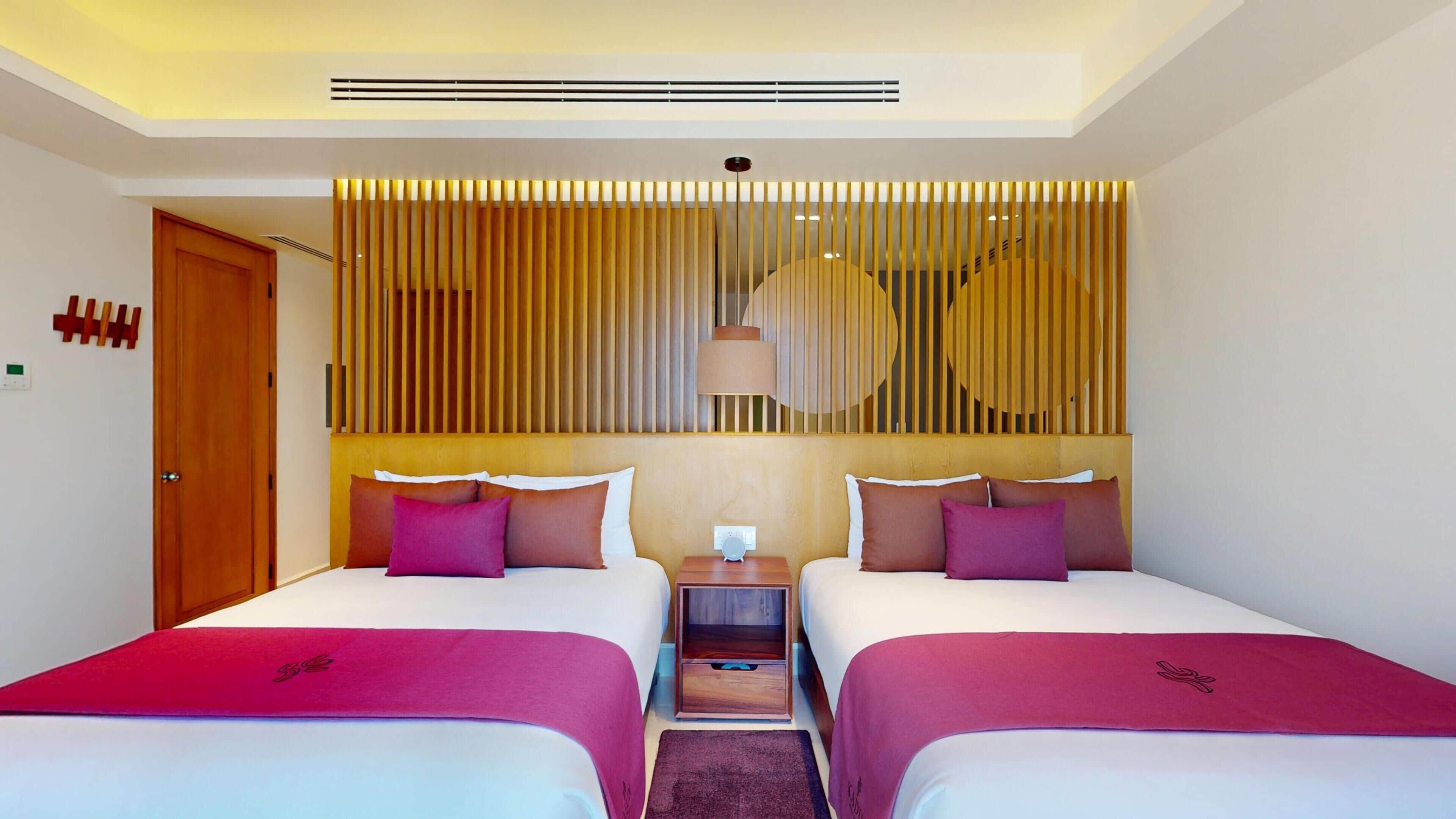 A hotel room with two beds, a wooden headboard, a nightstand, and a wall-mounted lamp.