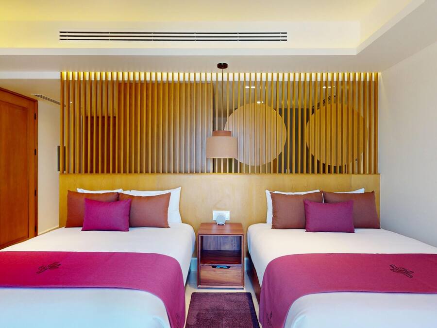 A hotel room with two beds, a wooden headboard, a nightstand, and a wall-mounted lamp.