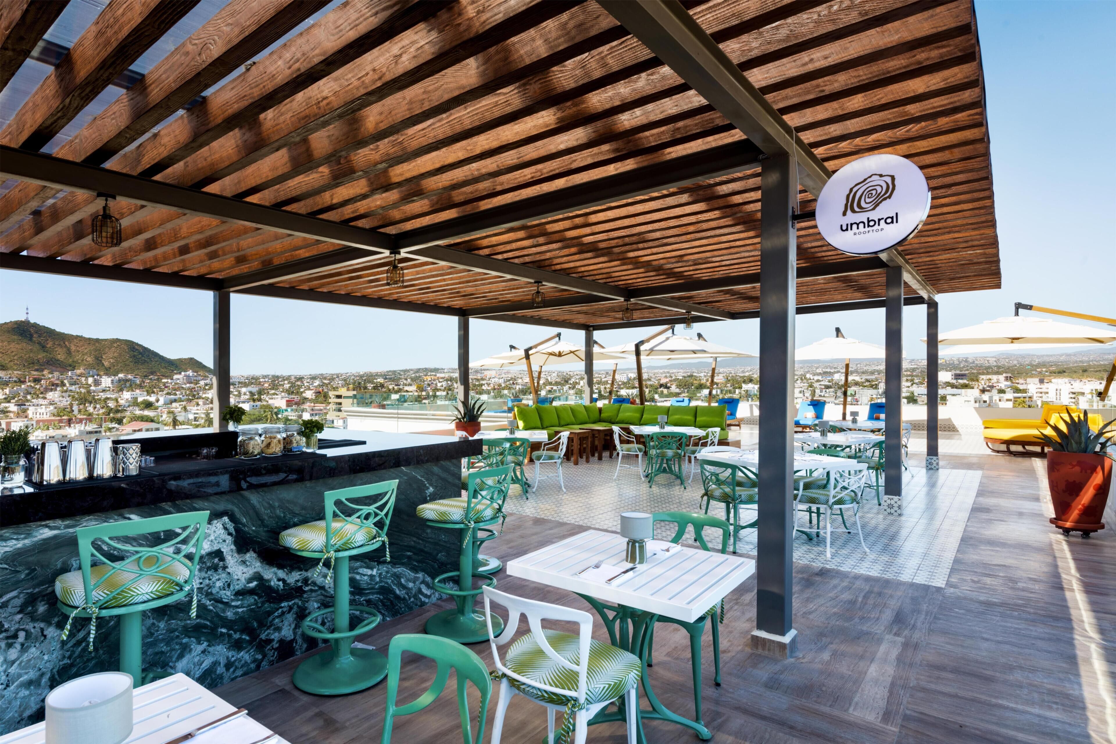 A rooftop bar with outdoor seating, a view of the city, and a wooden pergola.