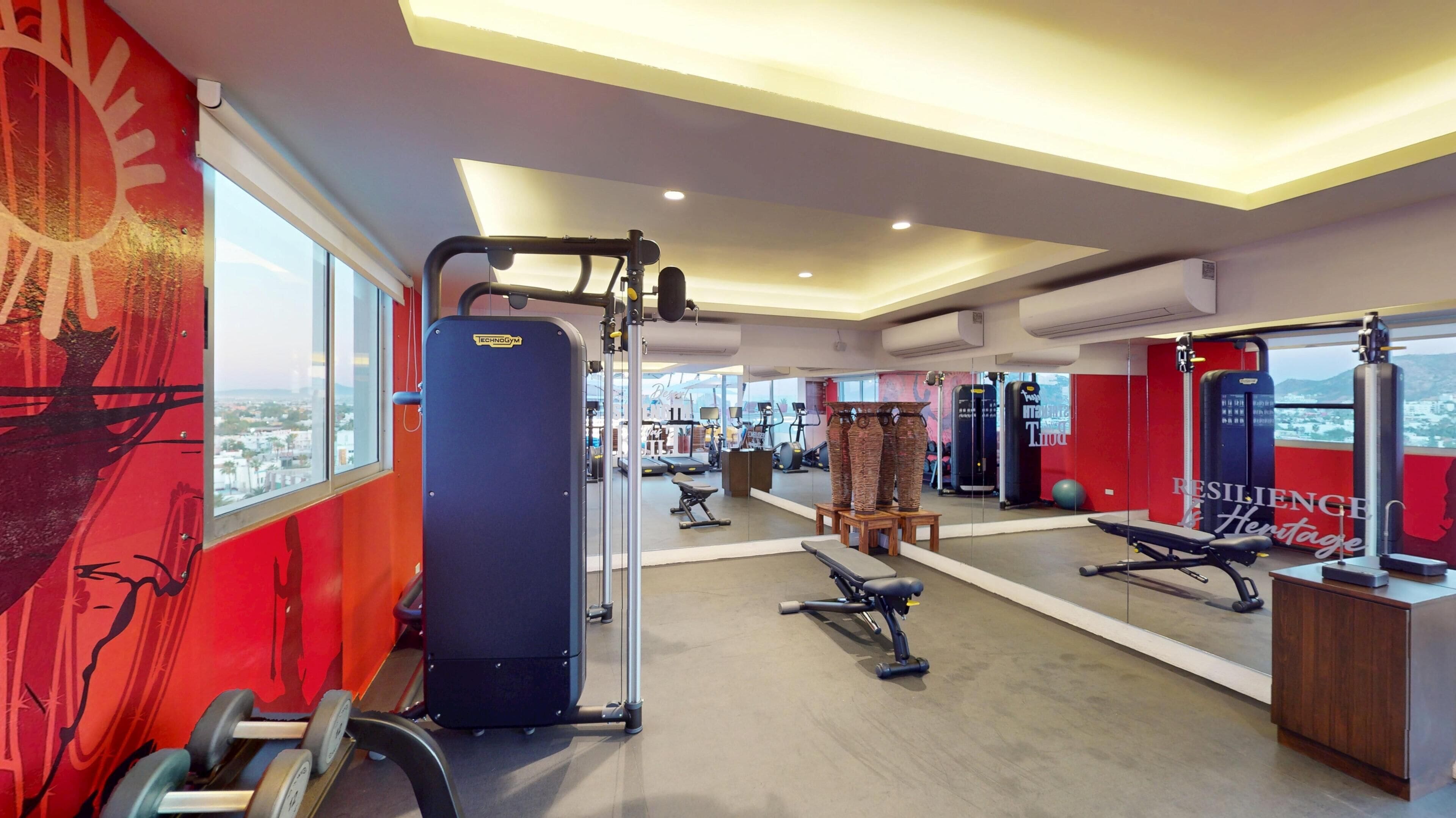 A gym with exercise equipment, a large mirror, and a view of a cityscape through large windows.