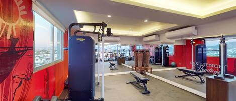 A gym with exercise equipment, a large mirror, and a view of a cityscape through large windows.