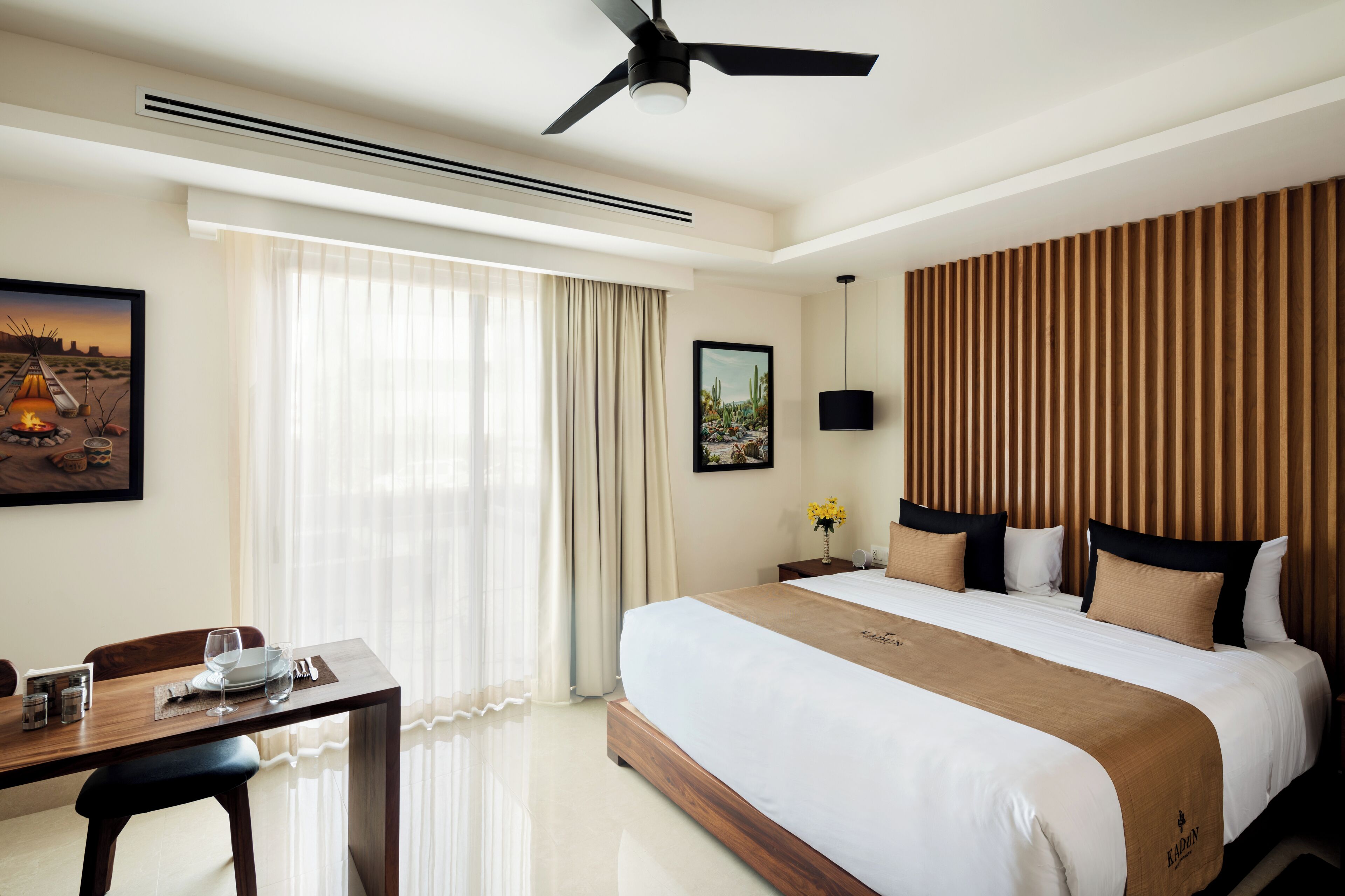 A hotel room with a large bed, a dining table, and a ceiling fan.