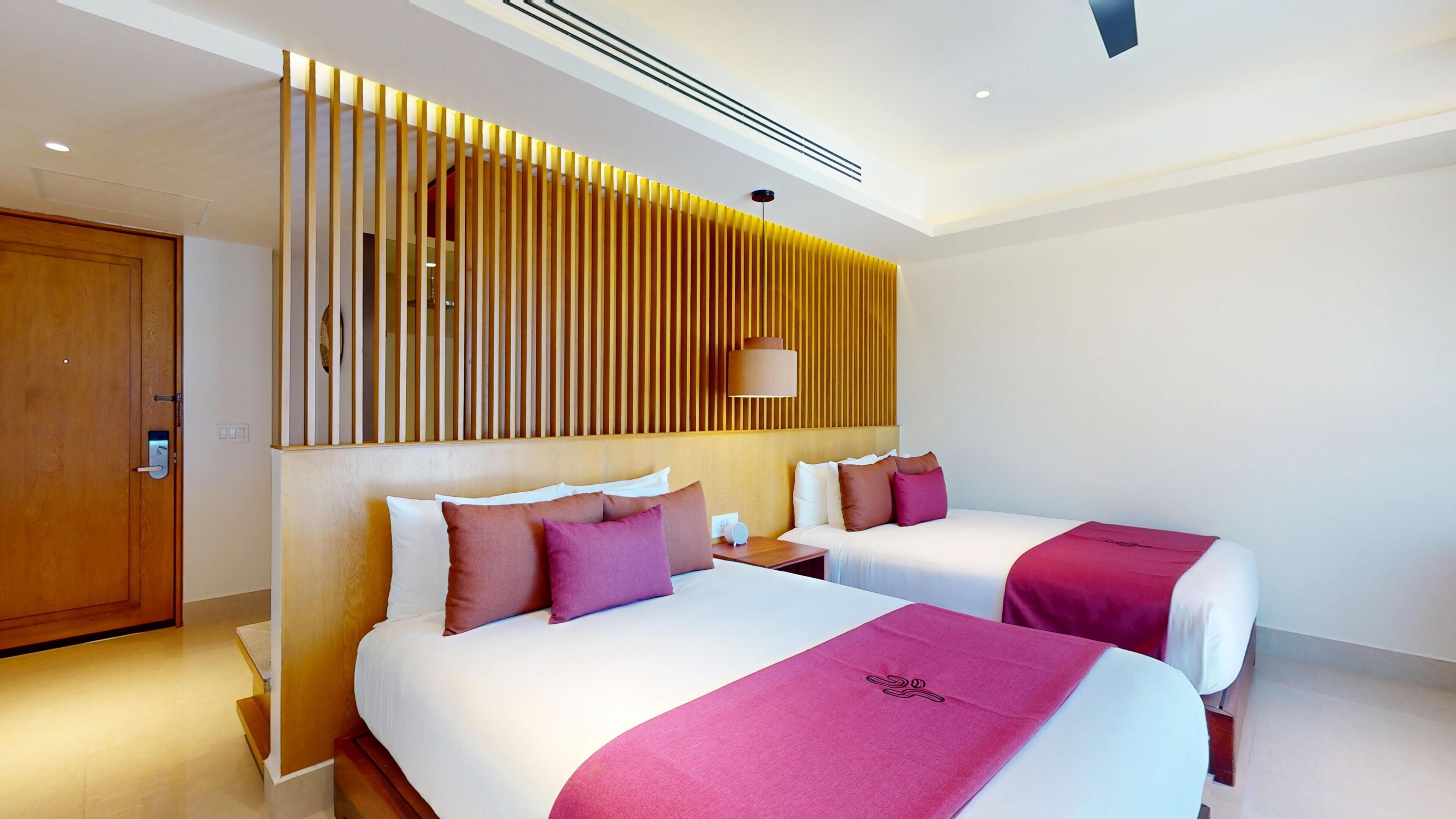 Ein Hotelzimmer mit zwei Betten, einer Holzhakenschubwand, einer Deckenleuchte und einer Tür.