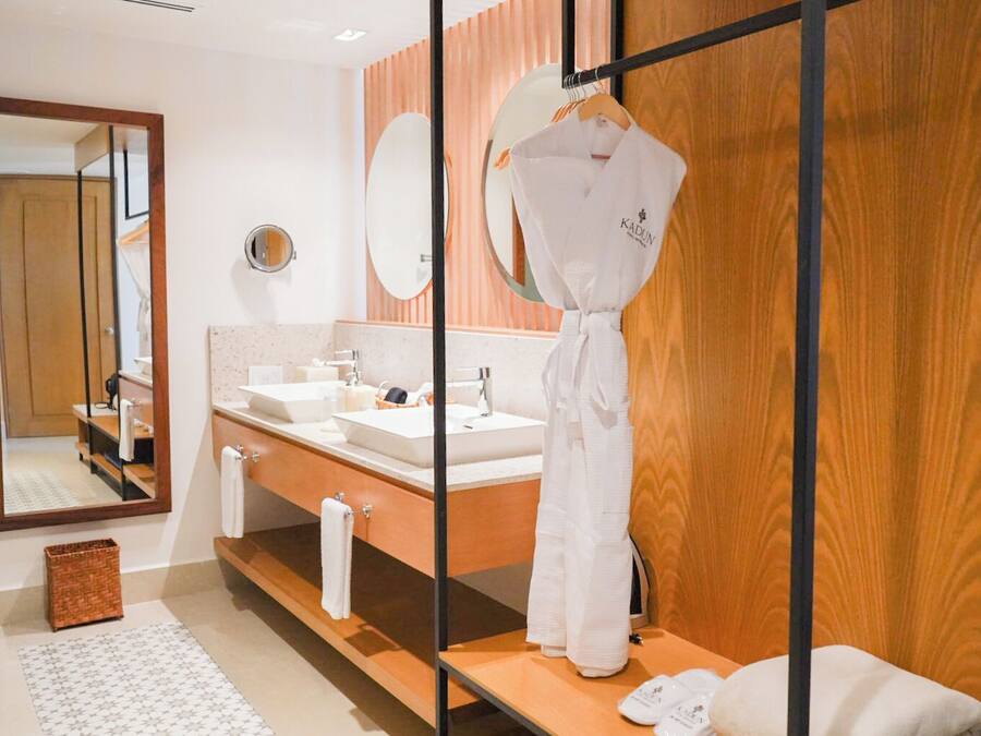 Een moderne badkamer met twee wastafels, een grote spiegel en een badjas die aan een houten rek hangt.