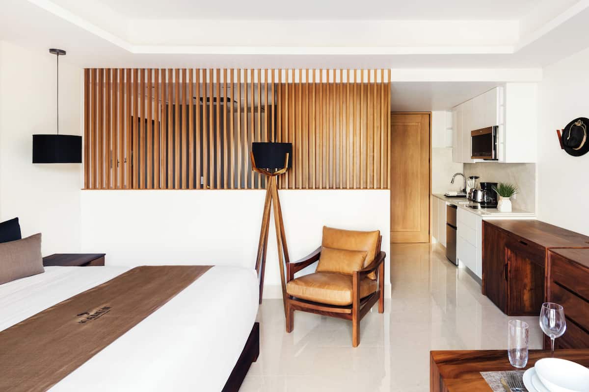 Een moderne hotelkamer met een groot bed, een houten scheidingswand, een bureau en een kitchenette.