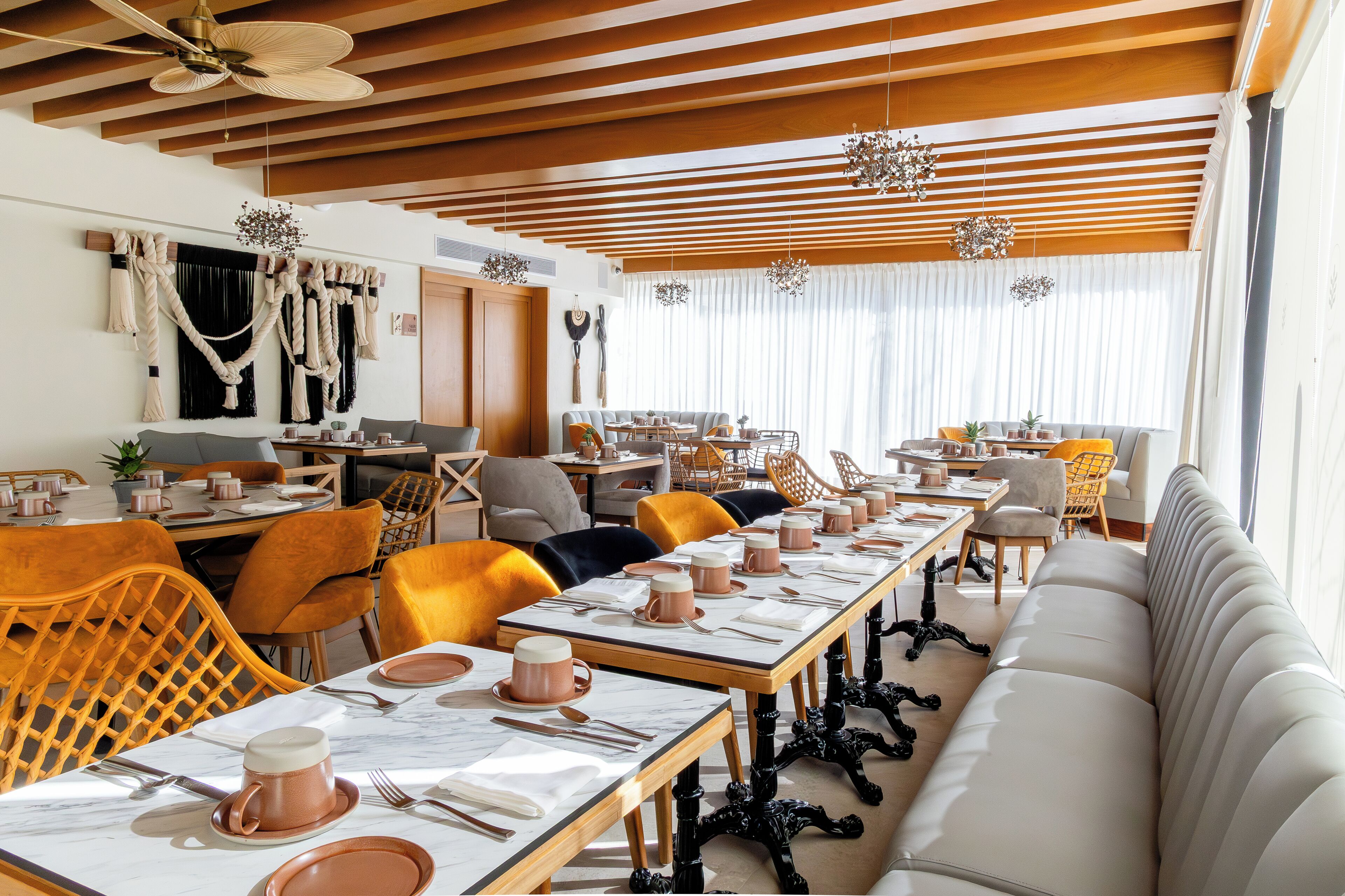 A modern dining area with wooden ceiling beams, a long table set for a meal, and a sofa along the wall.