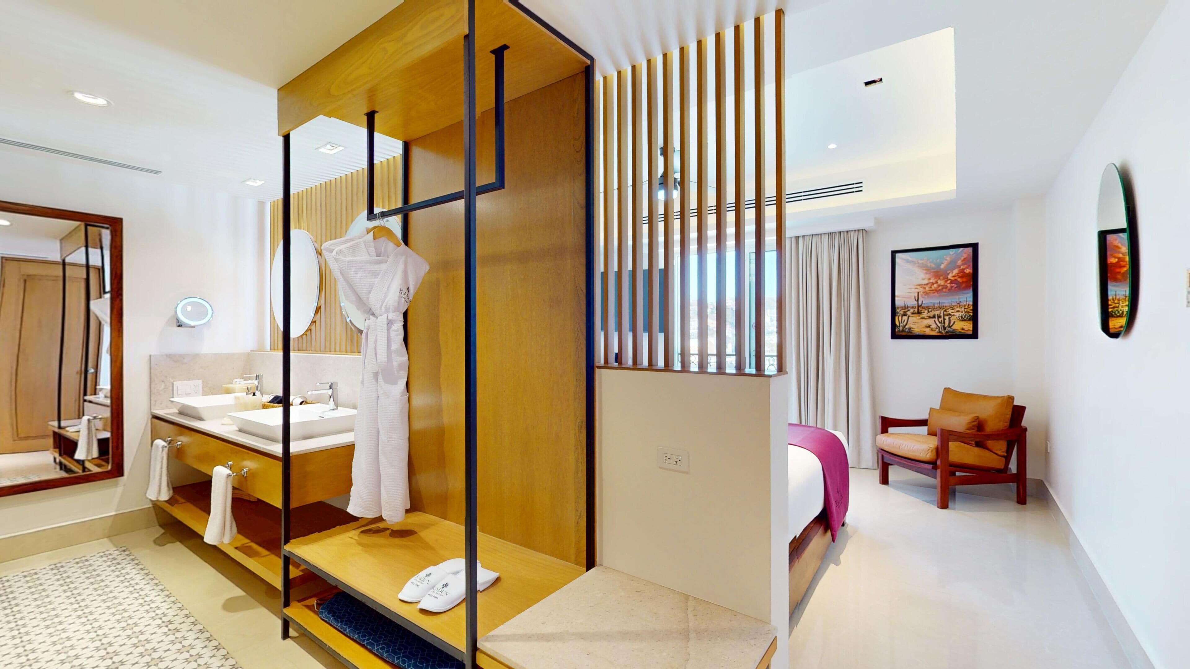 Une chambre d’hôtel moderne avec une cloison en bois, un grand miroir, un lit recouvert d’une couverture rose, une chaise et un tableau accroché au mur.