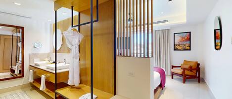Une chambre d’hôtel moderne avec une cloison en bois, un grand miroir, un lit recouvert d’une couverture rose, une chaise et un tableau accroché au mur.