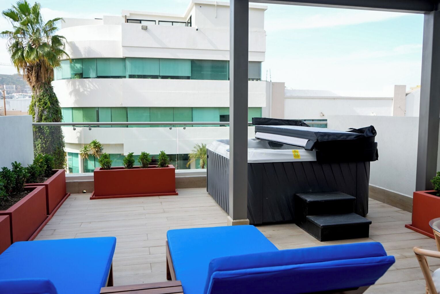 A rooftop terrace with blue lounge chairs, a hot tub, and potted plants.