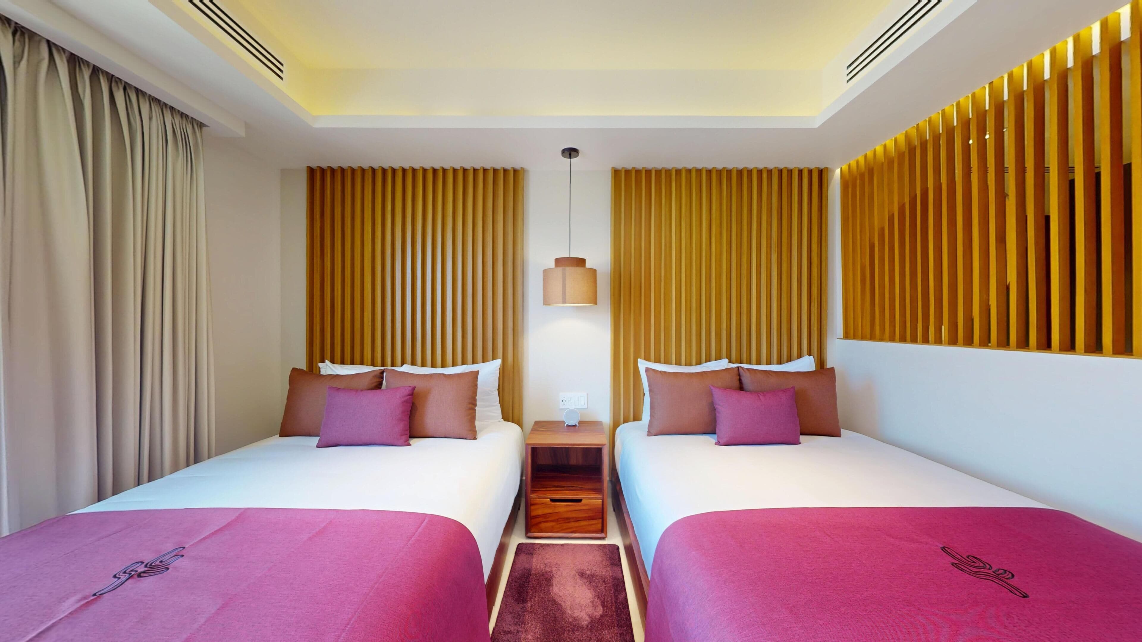 Una habitación de hotel con dos camas, una mesita de noche, una lámpara colgante y un cabecero de madera.