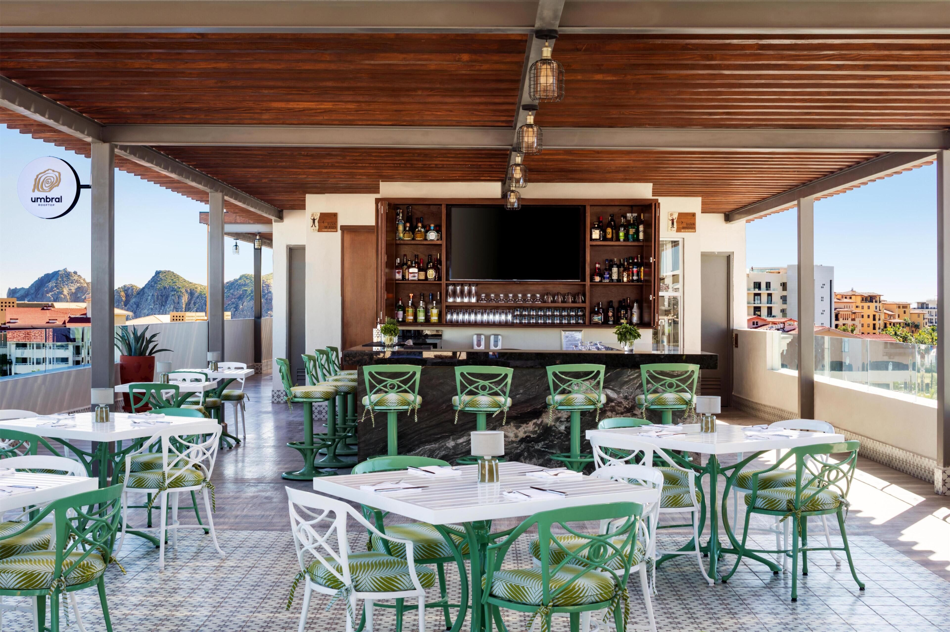 Eine Dachterrasse mit Holzboden, grünen Stühlen und einer Bar, die mit Flaschen bestückt ist.