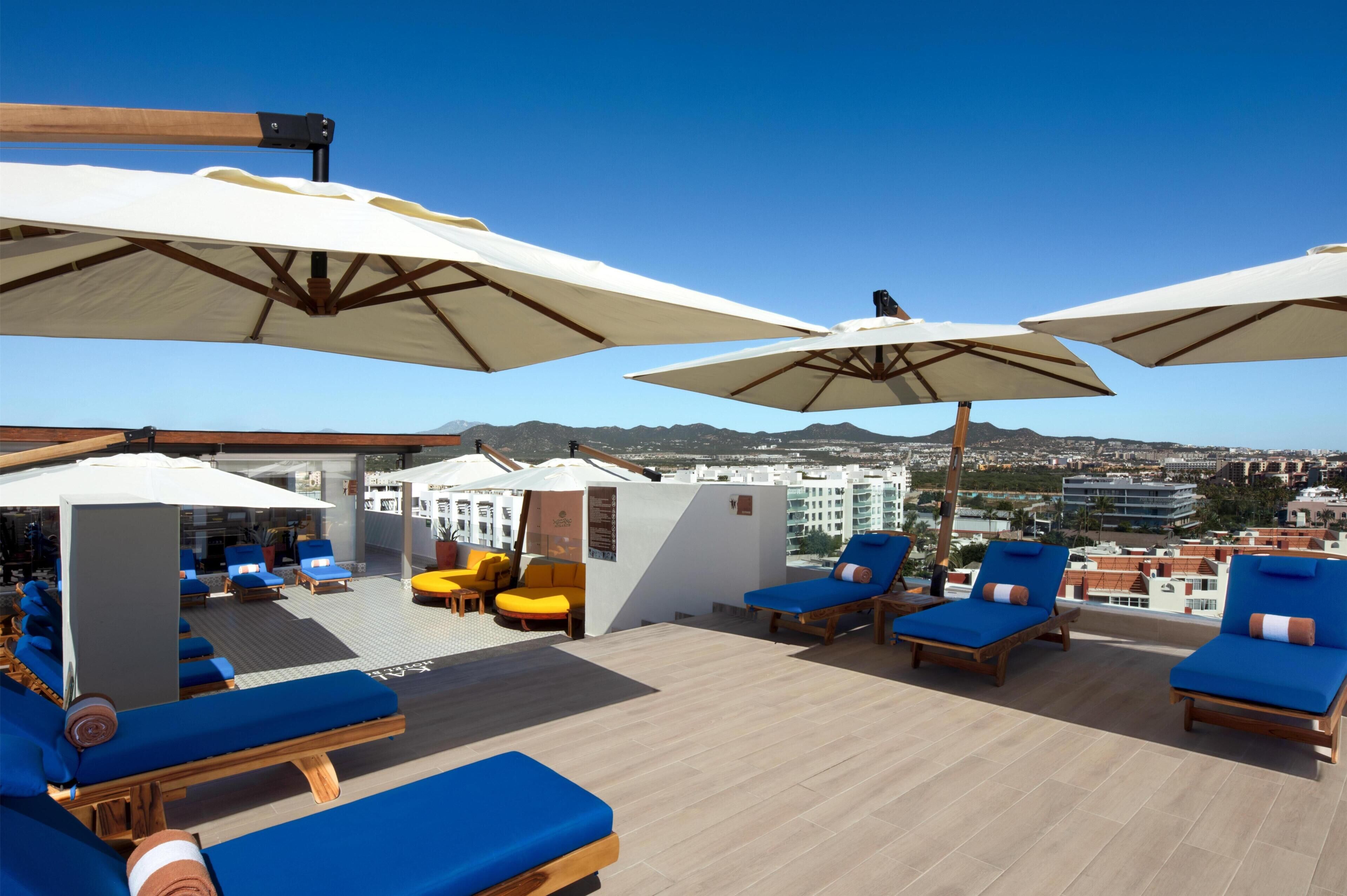 A rooftop lounge area with sun loungers, umbrellas, and a view of the cityscape.