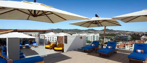 A rooftop lounge area with sun loungers, umbrellas, and a view of the cityscape.