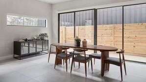 A dining area with a wooden table and chairs, a black cabinet, and a large window with a view of a wooden fence. - The Brown Oak: Nature & Splendor (Conroe)