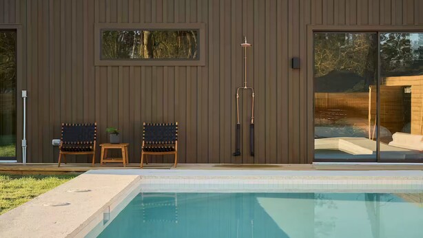 A modern house with a swimming pool, two wooden chairs, and a small table with a plant. - The Brown Oak: Nature & Splendor (Conroe)