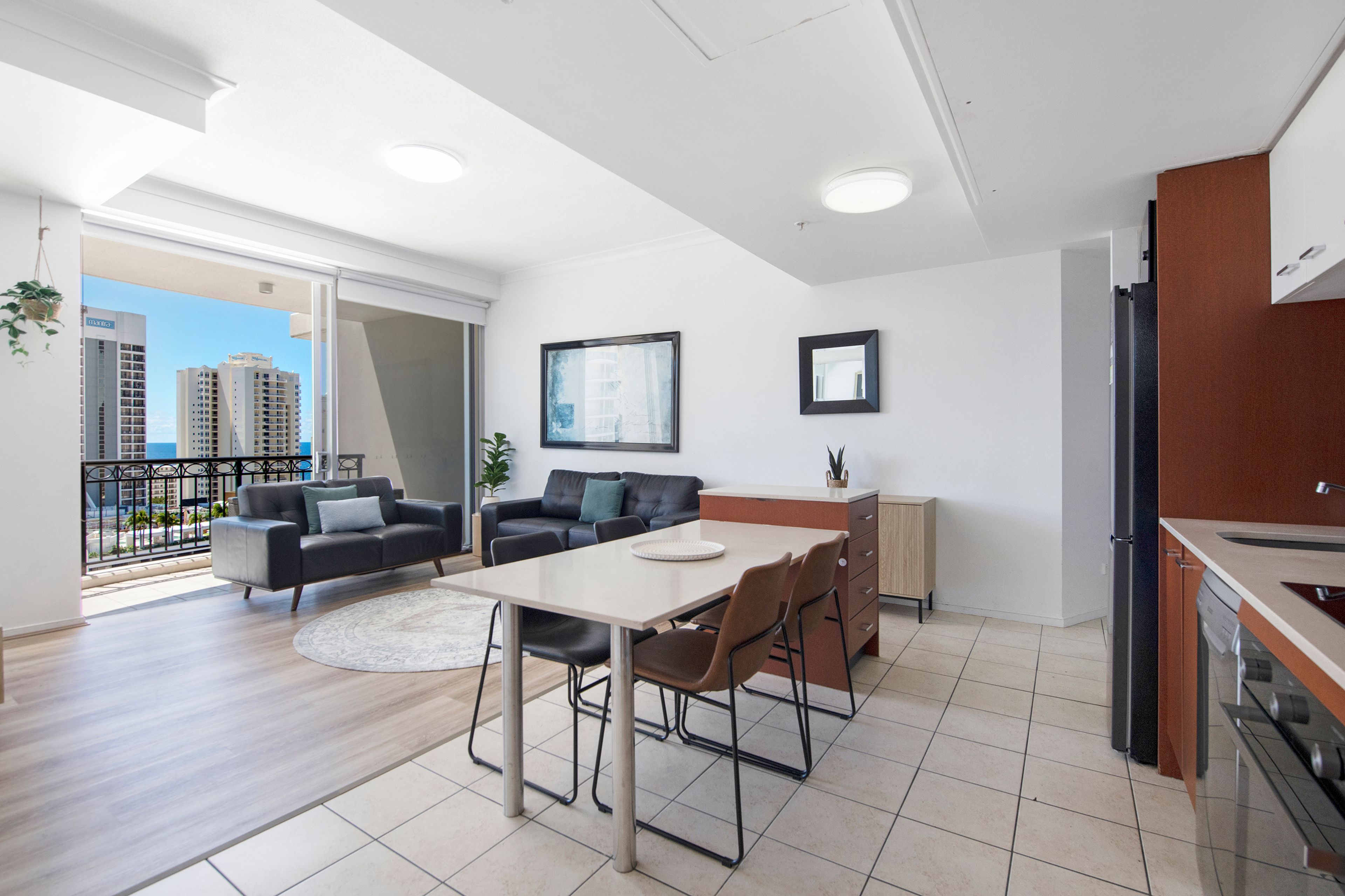 A modern apartment with a dining area, kitchen, and a balcony with a city view.