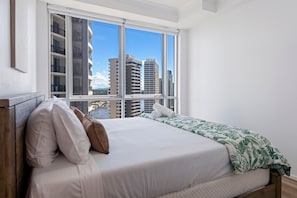 A hotel room with a bed, pillows, a window with a view of high-rise buildings and a body of water.
