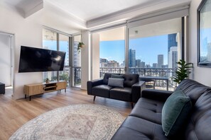 A modern living room with a large TV, leather sofa, and a view of the city skyline.