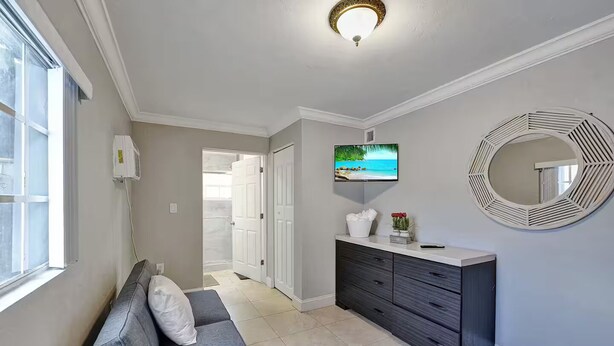 Un couloir moderne avec un canapé gris, un meuble en bois foncé, un téléviseur fixé au mur et un miroir décoratif.