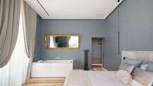 A modern bedroom with a large bed, a white bathtub, and a mirror on the wall.