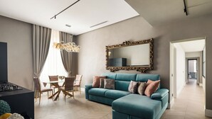 A modern living room with a teal sectional sofa, a dining area with a glass table, and a large ornate mirror on the wall.