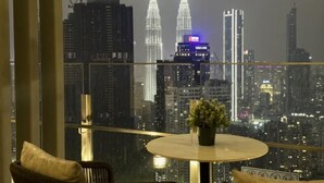 A room with a view of a city skyline, a round table with a vase, and a chair.