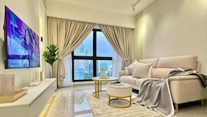 A modern living room with a sofa, a coffee table, a TV, and a large window with curtains.