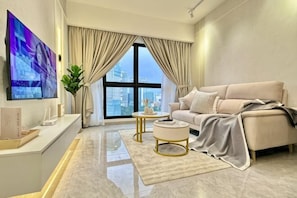 A modern living room with a sofa, a coffee table, a TV, and a large window with curtains.