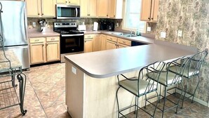 A kitchen with wooden cabinets, a stainless steel stove, a microwave, and a large island with bar stools.
