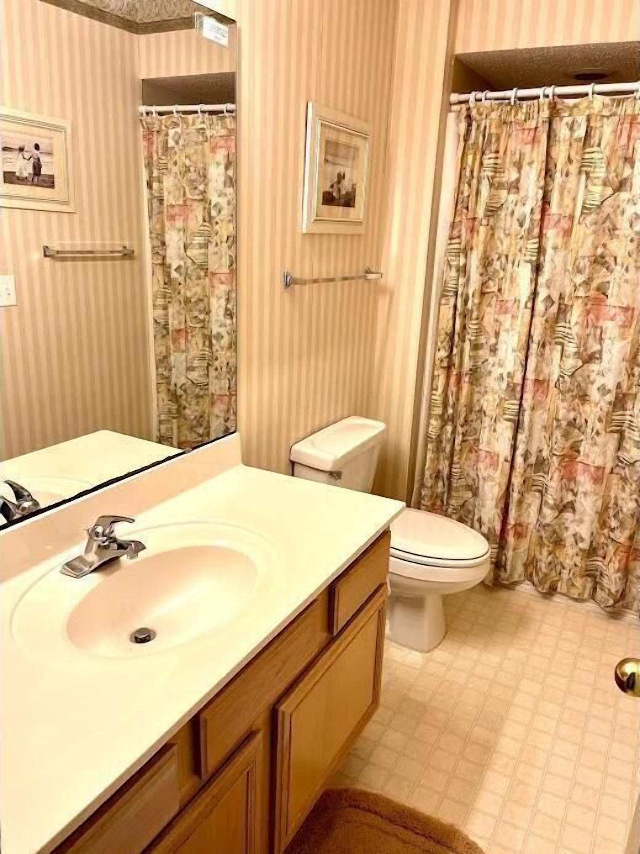 Ein Badezimmer mit Waschbecken, Spiegel, Toilette und Duschvorhang.