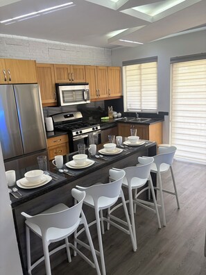 A modern kitchen with a central island, bar stools, stainless steel appliances, and wooden cabinets. - Dutch Village (Noord)
