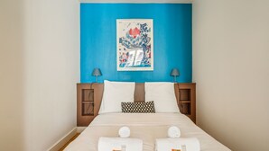 A hotel room with a bed, pillows, a blue wall, and a framed artwork.