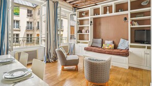 A modern living room with a wooden ceiling, a sofa with cushions, a TV, and a dining area with chairs and a table.