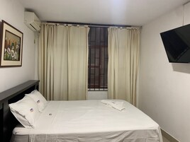 Habitación de hotel con cama, cortinas, televisor montado en la pared y ventana con reja de metal.