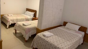 A hotel room with two single beds, a wooden headboard, a brick-patterned accent wall, and a tiled floor. - hostal regional (Piura)